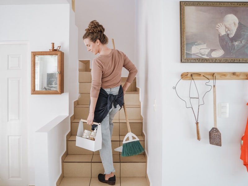 House cleaner carrying a cleaning caddy up the stairs of a home