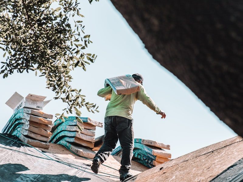 Roofer carrying a bundle of shingles across a roof